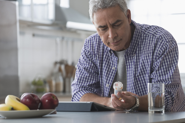 Hispanic man examining prescription bottle in kitchen